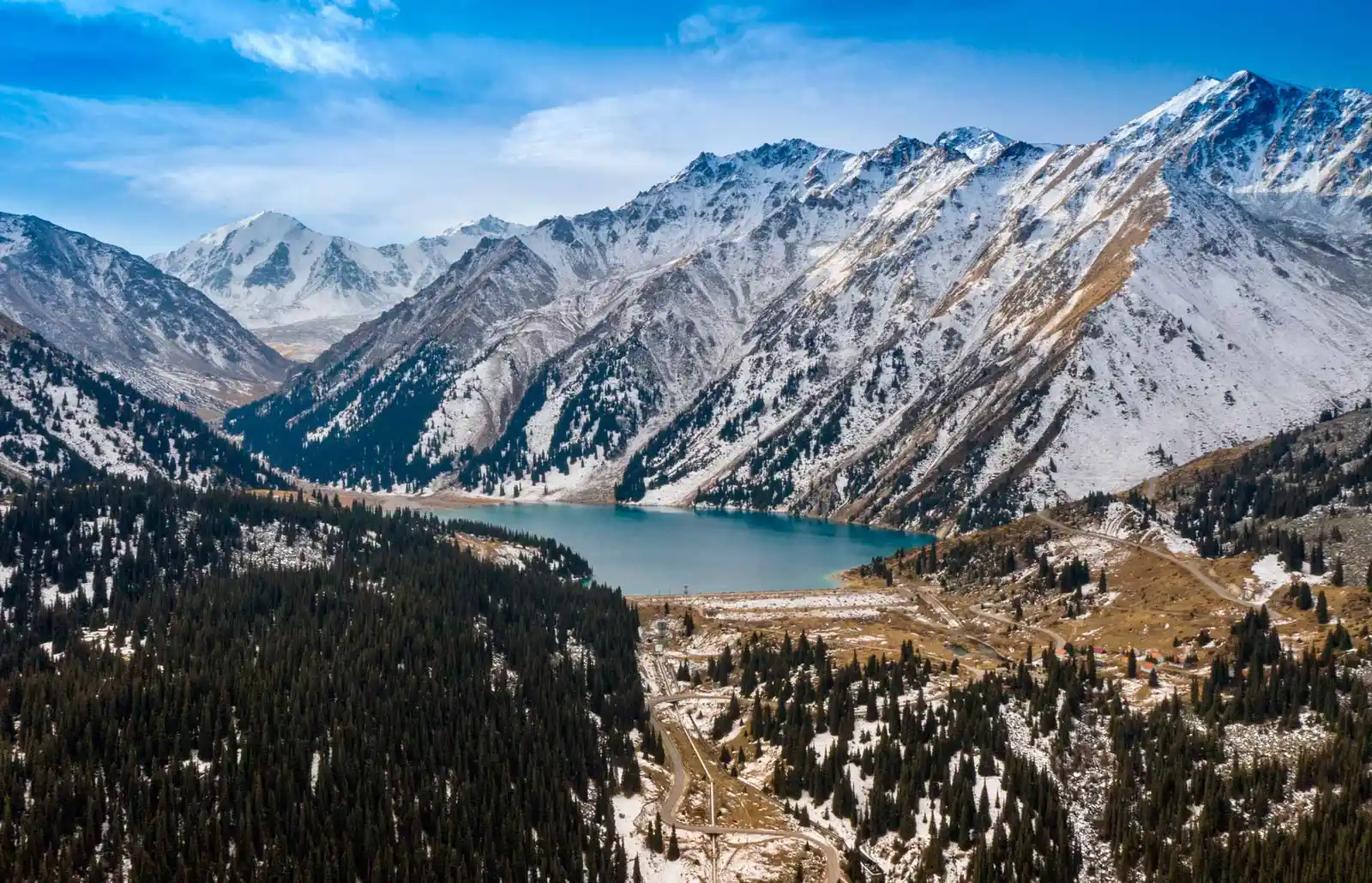 Aerial panorama of Big Almaty Lake with forested slopes, a mountain road and snowy peaks
